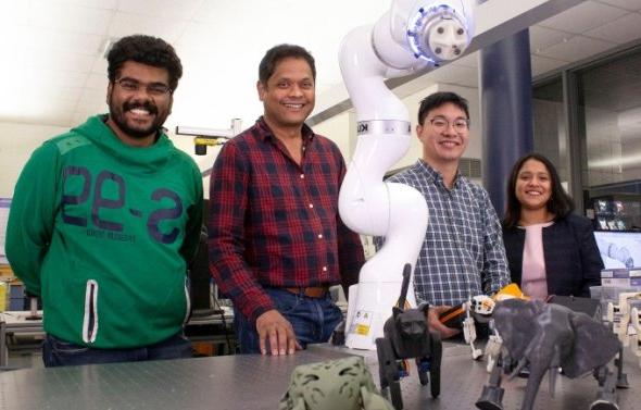 Group of engineering students standing next to robotic arm